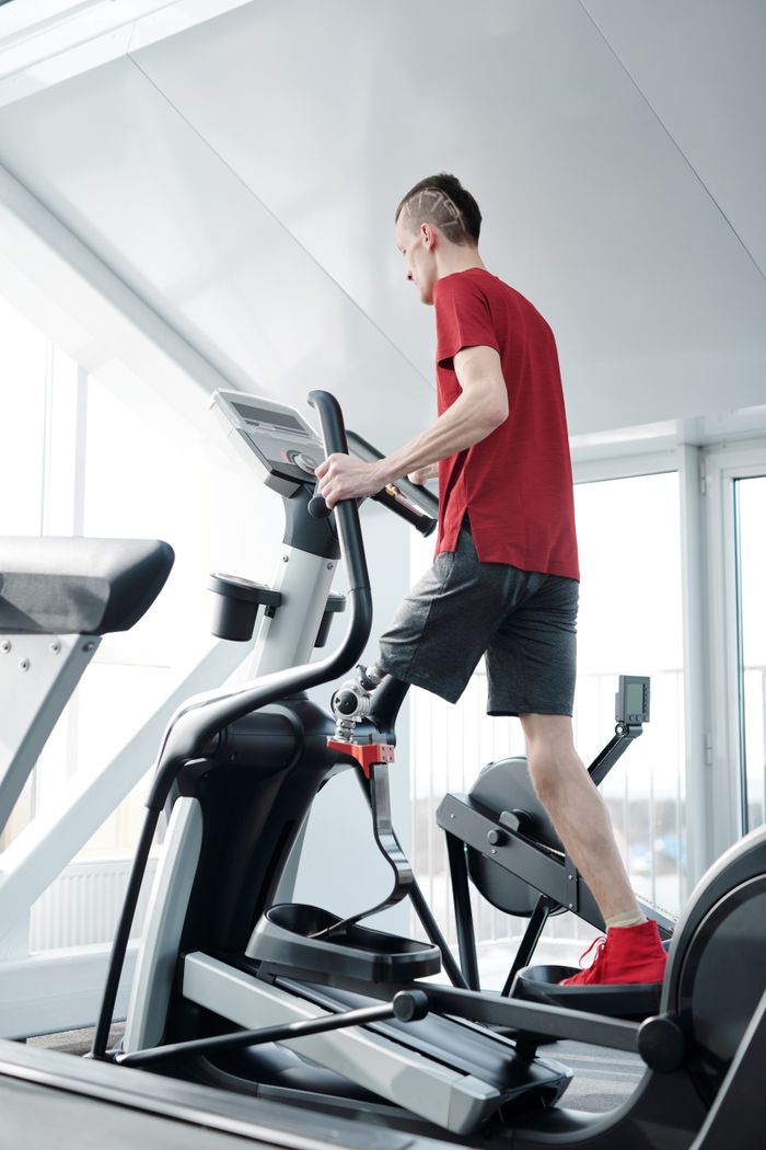 Man using an elliptical trainer in a gym wearing a prosthetic leg. Indoor fitness and health focus.
